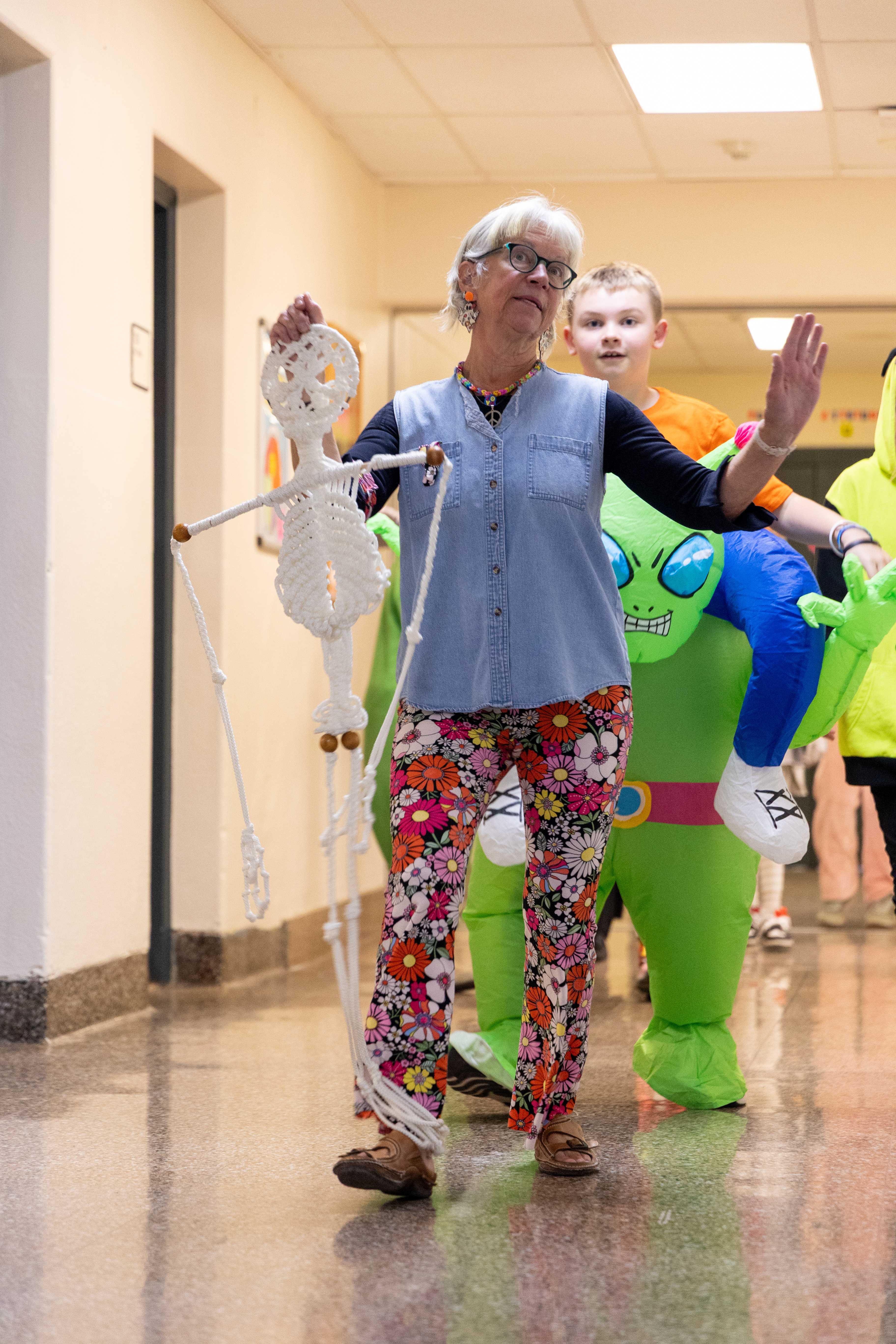 Ms. Patty dances in the hallway with other students, holding a skeleton on Halloween